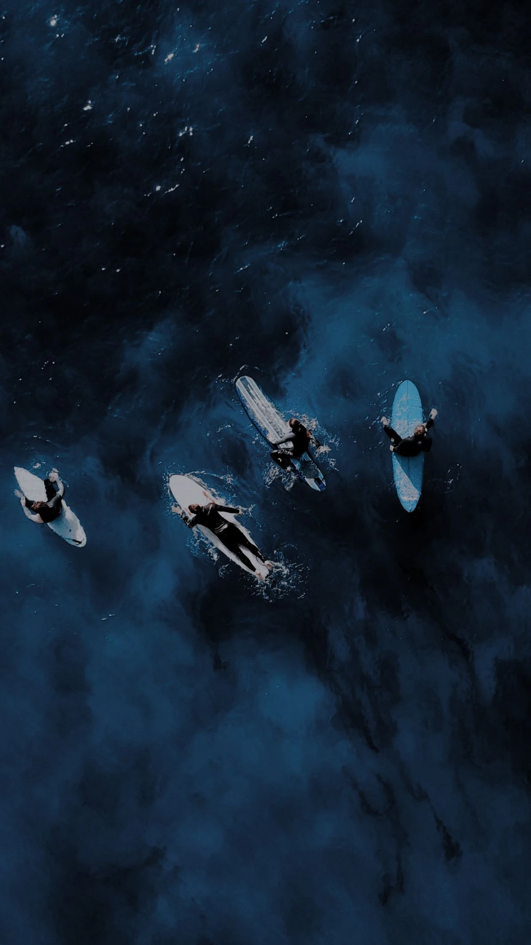 Surfers waiting in the lineup, seen from above on dark blue water