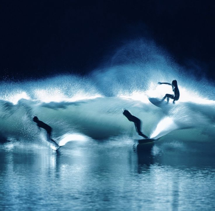 Surfers lit against a breaking wave at night